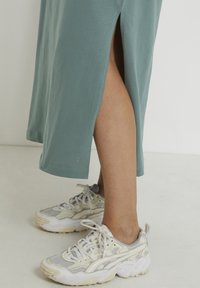 Light blue-green midi dress with side slits, paired with gray and white athletic sneakers featuring textured soles and prominent laces.