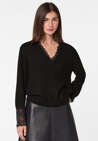 Schwarzer Pullover aus weichem Material mit V-Ausschnitt und dekorativem Spitzenbesatz. Spitze Akzente an den Ärmeln und lockerer Schnitt.