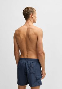 Mörkblå badbyxor med elastisk midja, en bakficka, slät yta och design som når en bit ovanför knäna.