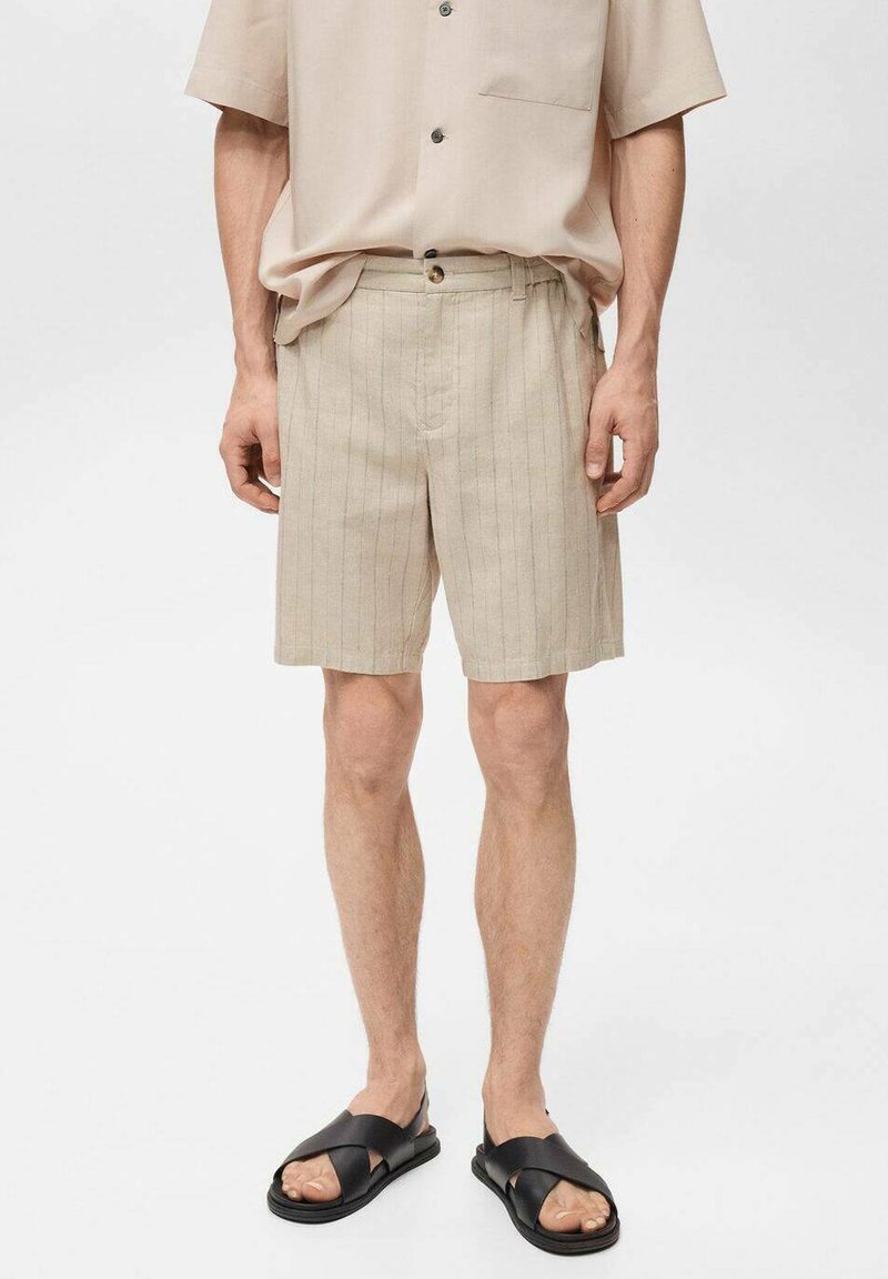 Beige linnen shorts met verticale strepen, voorzien van een knoopsluiting en zijzakken. Gecombineerd met zwarte instappers.