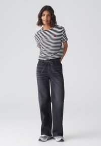 Striped black and white t-shirt with a red heart graphic, paired with dark denim wide-leg pants featuring a drawstring waist.