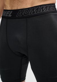 Približni prikaz osobe u uskim crnim sportskim šorcama s označenim pojasom marke "HUMMEL".