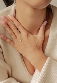 Srebrny naszyjnik z małymi okrągłymi zawieszkami, prezentowany na tle kremowego swetra dzianinowego. Delikatny wzór łańcuszka podkreśla prostą elegancję.