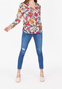 Blusa floreale con scollatura a V, maniche lunghe e sfondo crema. Abbinata a jeans skinny blu e scarpe espadrillas beige chiaro.