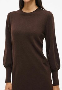 Bruine gebreide sweaterdress met een ronde halslijn, lange poffende mouwen en geribbelde boorden. Zachte textuur, aansluitend ontwerp.