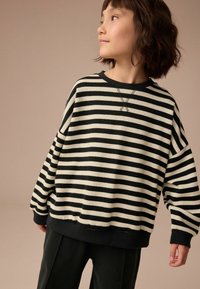 Sweatshirt noir et crème à rayures, avec une coupe décontractée, des poignets côtelés et un large col. Texture douce avec un détail de couture décoratif.