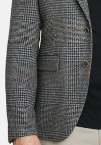 Blazer a cuadros texturizado en navy, marrón y crema. Presenta dos botones de tono dorado, un bolsillo en el pecho y un corte clásico.