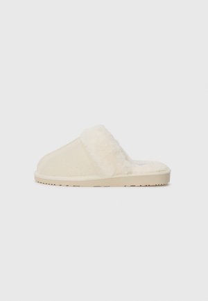 Zapatillas de casa de pelaje sintético beige con una textura suave, diseño de espalda abierta y suela de goma plana. Silueta minimalista y color neutro.