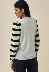 Sweatshirt gris clair avec des manches rayées noires et grises, présentant un col rond et un ourlet côtelé, vu de dos.