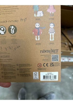 Verpakking met illustraties van poppen in verschillende outfits (lente, zomer, herfst, winter) met aardse tinten op een bruine achtergrond.