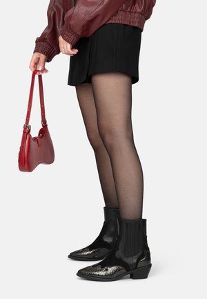 Bottines noires avec un bout en cuir brillant à motif serpent, des panneaux texturés, en cuir, assorties à une jupe noire et un sac à main rouge.