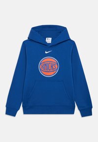 Modrá mikina s kapucí vyrobená z měkké tkaniny, se přední kapsou. Má kulatý logo s textem "KNICKS" a nad ním ikonický znak Nike.