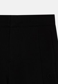 Sorte leggings med en jevn tekstur, med subtile stikking detaljer og en preget logo på høyre side.