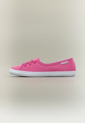 Nízký růžový teniska s bílou podrážkou a tkaničkami, štítek Lacoste na boku, na jednoduchém světlém pozadí.