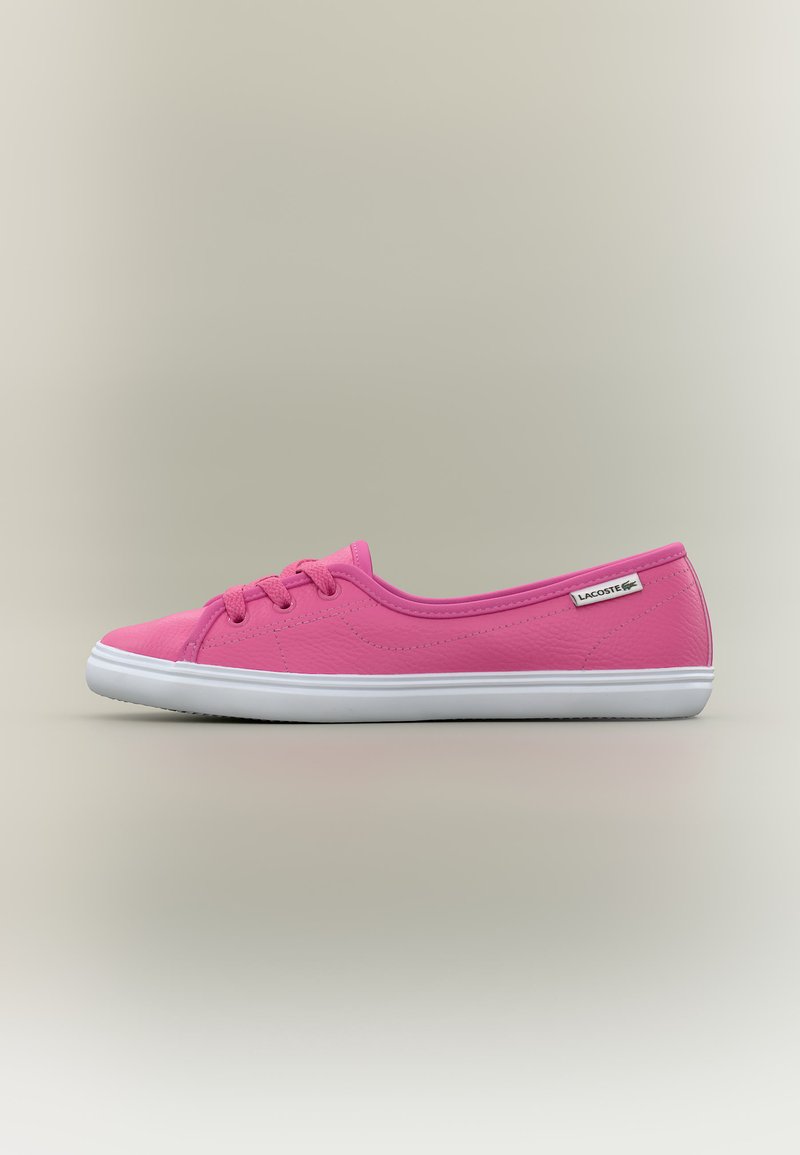 Zemas profilētas rozā sporta kurpes ar baltu zoli un šņorēm, Lacoste etiķete sānos, uz vienkārša gaiša fona.