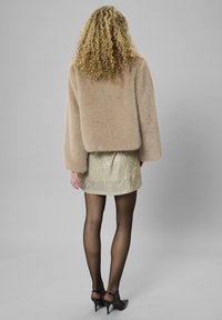 Napa jakna iz umetnega krzna v bež barvi, sproščenega kroja, v kombinaciji z bleščečo zlatno mini krilom, črnimi prosojnimi nogavicami in črnimi špicastimi petkami.