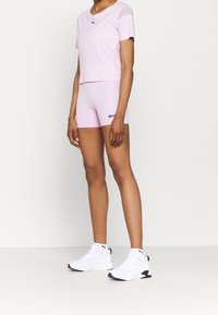 Ljusrosa tränings T-shirt med korta ärmar och logotyp, som matchas med rosa shorts. Avslutas med vita och svarta träningsskor.