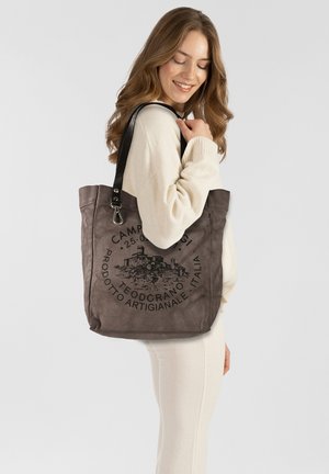 Graue Tragetasche mit schwarzem Aufdruck, der ein architektonisches Design zeigt. Hergestellt aus weichem Material, verfügt sie über einen Lederriemen und eine quadratische Form.