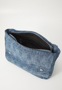 Bolso de mano de mezclilla con un exterior azul texturizado, cierre de cremallera y interior negro. Cuenta con dos botones de presión metálicos en la parte frontal.