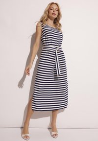 Niebieska i biała sukienka w paski z bezrękawowym fasonem, z pasa z klamrą w kolorze złotym i bocznymi rozcięciami. Gładka tekstura materiału.