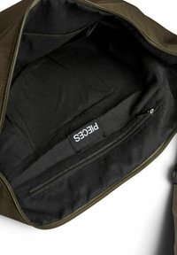 Ciemnozielona torba z przedziałem zamykanym na zamek. Wnętrze wyłożone czarną tkaniną z małą metką. Charakteryzuje się gładką fakturą i minimalistycznym designem.