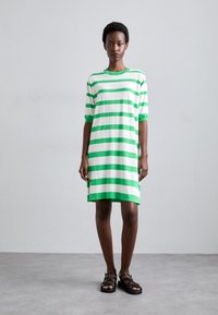 Abito a t-shirt in cotone a righe verde e bianco, con maniche corte e una vestibilità rilassata, che arriva a metà coscia. Indossato con sandali neri.
