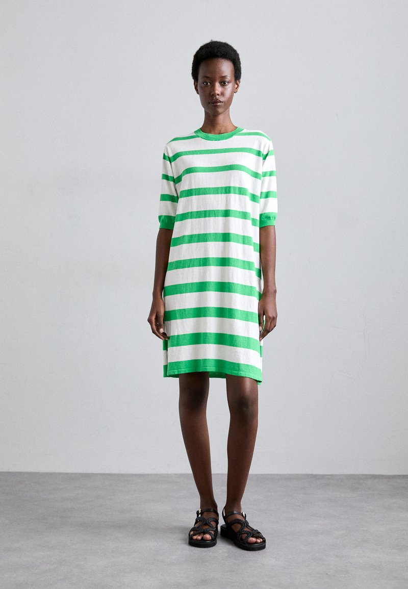 Abito a t-shirt in cotone a righe verde e bianco, con maniche corte e una vestibilità rilassata, che arriva a metà coscia. Indossato con sandali neri.