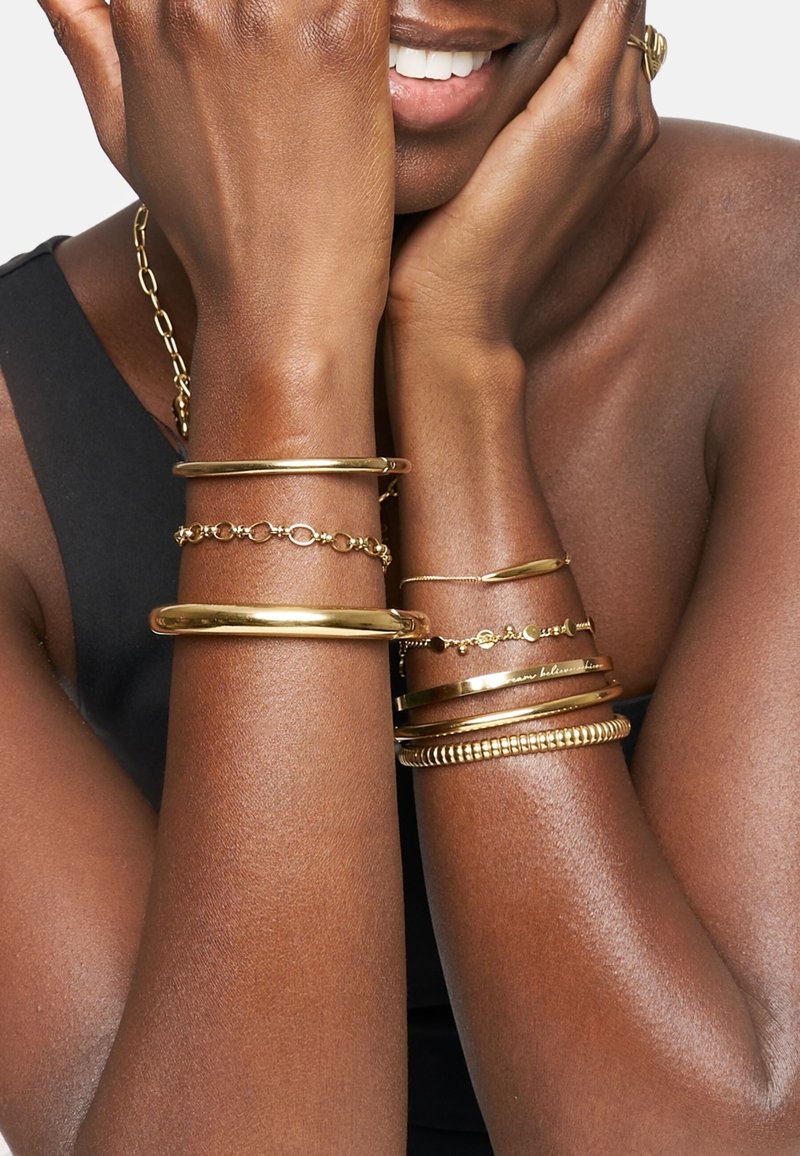 Set goldener Armbänder in verschiedenen Designs: zwei glatte Bangles, eine verlinkte Kette, ein schlanker Balken und eine genoppte Textur.