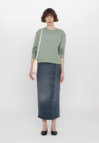 Zelená mikina s nápisem "ARMANI EXCHANGE" v lesklých písmenech, zkombinovaná s tmavými denimovými maxi sukněmi a černými balerínami, s malou bílou kabelkou.