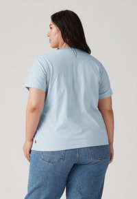 Ανοιχτό μπλε βαμβακερό t-shirt με κοντά μανίκια και στρογγυλή λαιμόκοψη, με μια μικρή κόκκινη ετικέτα στο τελείωμα. Λεία υφή, άνετη εφαρμογή.