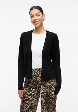 Black cardigan with open front design, ribbed cuffs, and soft texture, worn over a white shirt and paired with leopard print pants.