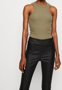 Olive green ribbed tank top with a high neckline, paired with black faux leather high-waisted pants. Smooth texture with fitted design.