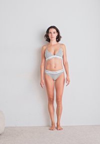 Grijze katoenen bralette en bijpassende bikini met elastische tailleband, voorzien van een witte logoband. De outfit is minimalistisch en naadloos van ontwerp.