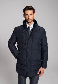 Granatowa puchowa kurtka z wysokim kołnierzem, zapięciem na guziki i pikowaną teksturą. Została zaprojektowana z bocznymi kieszeniami i eleganckim, dopasowanym krojem.