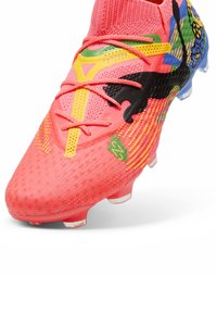 Scarpe da calcio di un brillante colore corallo con una tomaia testurizzata, accenti colorati e lacci. Presenta un motivo distintivo e una suola stampata con più tacchetti.