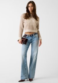 Maglione corto beige chiaro lavorato a maglia con dettagli testurizzati, abbinato a jeans azzurri a vita alta e gamba dritta e a una borsa bordeaux.