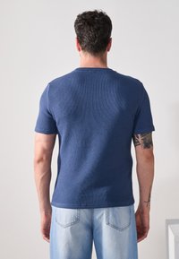 Marineblå strikket t-skjorte med korte ermer og teksturert mønster, rund hals og noe løs passform, kombinert med lyseblå denimjeans.