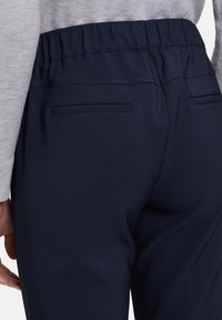 Námořnické kalhoty s elastickým pasem a hladkým povrchem, se dvěma zadními kapsami a švy, v kombinaci se šedým svetrem.