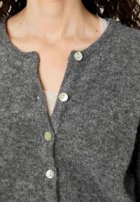 Šedý vlněný cardigan s výstřihem do V, se pěti světlými knoflíky a texturovaným povrchem. Měkká a teplá tkanina, částečně zapnutá.
