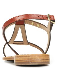 Bruine leren sandalen met een lichte voetbed, voorzien van een lusvormig bandenontwerp, een slank profiel en een platte houten zool. Goudkleurige gesp detail.