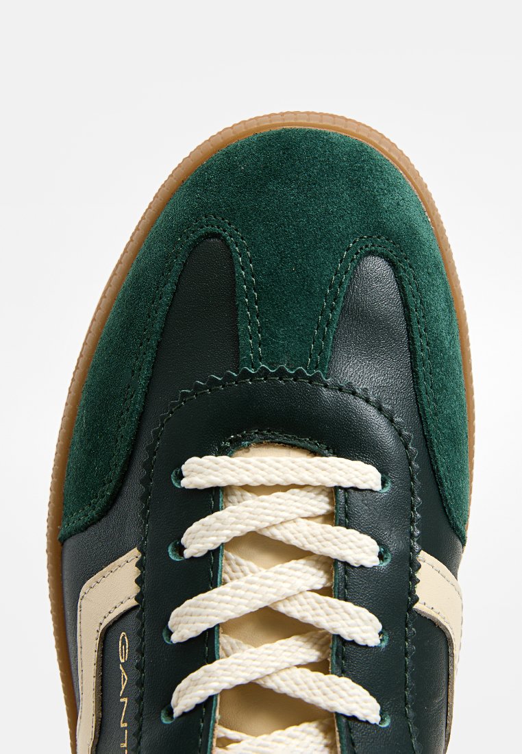 Zielone zamszowe i skórzane trampki z kremowymi sznurówkami, tanową gumową podeszwą oraz dekoracyjnym wykończeniem na palcach i bokach.