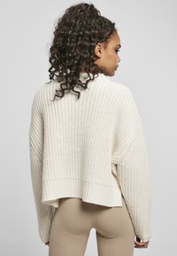 Pull en maille de couleur crème avec un design court, un ourlet côtelé et un motif texturé. Présente des épaules tombantes et des manches longues.