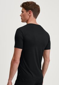 Black short-sleeve t-shirt made of soft fabric; features a crew neck and a small button accent at the back, with a smooth texture.