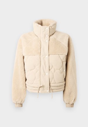 Chaqueta acolchada beige con cuello alto, cuerpo acolchado y mangas de sherpa suaves y texturizadas. Cuenta con botones a presión y un dobladillo ajustable.