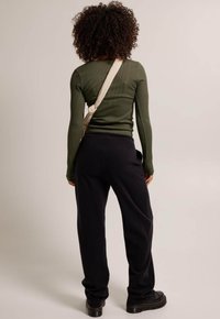 Olive ribbed long-sleeve top, black loose-fitting sweatpants, paired with chunky black boots, and a cream crossbody bag.