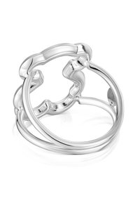 Dos anillos plateados brillantes entrelazados, uno de ellos con un diseño ondulado y orgánico, exhibidos sobre una superficie blanca reflectante.