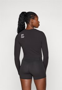 Haut noir à manches longues et short ajusté en tissu lisse. Le haut présente un texte blanc sur le dos indiquant "WORLD SERIES OF FITNESS RACING".