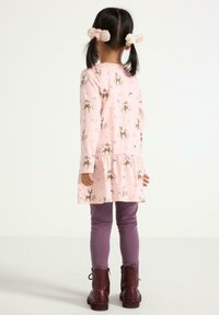 Lyserød langærmet kjole med rensdyr- og blomstertryk, lagdelt kant, parret med lilla leggings og sorte ankelstøvler.