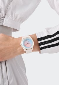 Valge kell, millel on ümar korpus ja helesinise-roosa gradient dials. Omab kahte õhukest käe ja tekstuuriga valget silikoonriba.