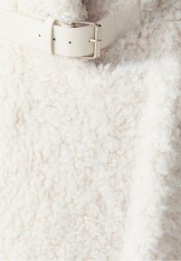 Tela blanca texturizada con un aspecto esponjoso, que presenta un cinturón de cuero de color claro y detalles de hardware plateado para el cierre.